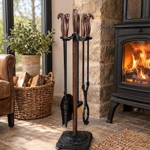 May include: A fireplace tool set featuring a central stand with a square black base and a copper-toned pole. The set includes a shovel, a brush, and tongs, each topped with a detailed bronze-colored eagle head handle design.