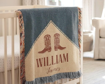 May include: A woven throw blanket featuring a blue and beige triangular design with a pair of brown cowboy boots, the name WILLIAM in block letters, and the name James in script, finished with multicoloured fringe on the sides.