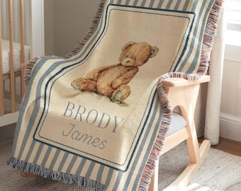May include: A beige and blue striped baby blanket with a teddy bear illustration and the name "BRODY James" in blue lettering. The blanket is draped over a wooden rocking chair.