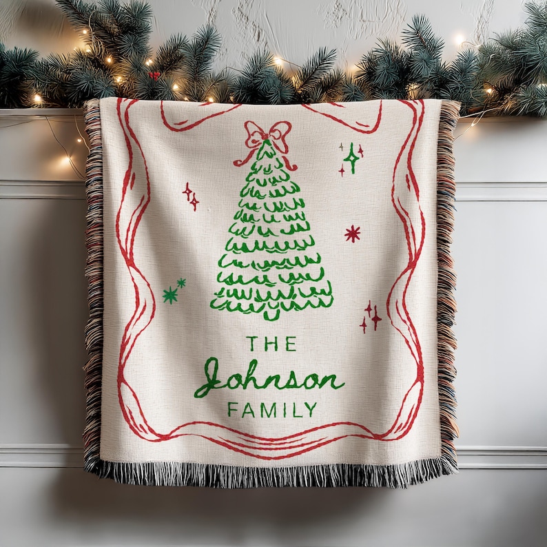 May include: Cream-colored woven throw blanket with a red border and fringe. A green Christmas tree design is centered, with the text "THE JOHNSON FAMILY" in green. Festive holiday decor.