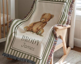 May include: A personalized baby blanket draped over a wooden rocking chair. The blanket features a brown teddy bear illustration and the name "BRODY James" in script. The blanket has green and white stripes and fringe.