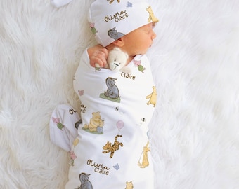May include: A newborn baby swaddled in a white blanket and matching hat, both adorned with Winnie the Pooh characters. The blanket and hat feature illustrations of Pooh, Tigger, Eeyore, and other characters. The name "Olivia Claire" is printed on the hat and blanket.