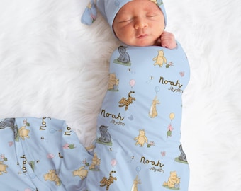 May include: A baby swaddled in a light blue blanket and matching hat, both adorned with Winnie the Pooh characters and the names "Noah Jayden". The blanket and hat feature illustrations of Pooh, Tigger, and other characters.