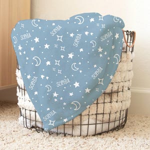 May include: A light blue baby blanket with a white moon and star pattern. The blanket has the name "Sophia" repeated throughout the design.