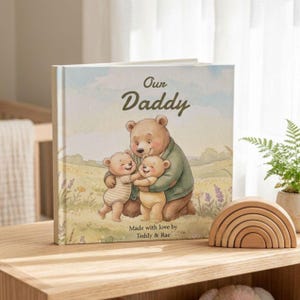 May include: A children's book titled "Our Daddy" with a watercolor illustration of a bear family. The cover features a bear embracing two smaller bears. A wooden rainbow toy sits beside the book on a wooden surface.