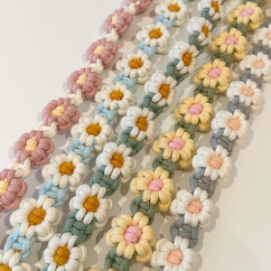 Puede incluir: Cinco pulseras de crochet de flores de margarita de colores en tonos de rosa, azul, verde, amarillo y gris. Las pulseras están hechas con un patrón simple de flor de margarita y son perfectas para agregar un toque de fantasía a cualquier atuendo.