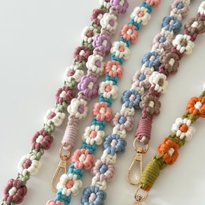 May include: Four colorful macrame straps with flower designs and gold clasps. The straps are made with different colored yarn and feature a variety of flower shapes.
