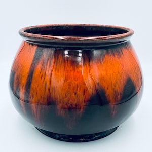 Peut inclure: Un bol en céramique rond doté d'un vernis brillant avec un motif goutte à goutte orange vif et noir profond. Le récipient présente une large ouverture et un corps lisse et incurvé qui se rétrécit vers une base circulaire, aux tons fondus.