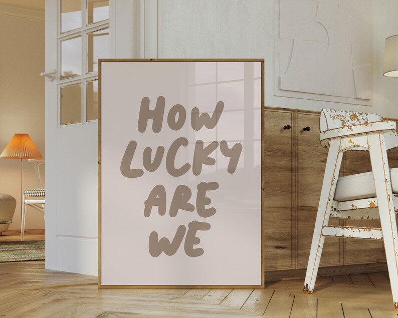 Puede incluir: Una impresi&oacute;n enmarcada con el texto "How lucky are we" en marr&oacute;n sobre un fondo blanco.