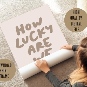 Puede incluir: Una descarga digital de un p&oacute;ster imprimible con el texto "How lucky are we" en marr&oacute;n sobre un fondo rosa claro. El p&oacute;ster est&aacute; enrollado y lo sostiene una mano. El texto "Download, Print, Frame" est&aacute; en un rect&aacute;ngulo marr&oacute;n en la esquina inferior izquierda del p&oacute;ster. El texto "High Quality Digital File" est&aacute; en un c&iacute;rculo marr&oacute;n en la esquina superior derecha del p&oacute;ster.