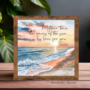 Op de afbeelding: Een ingelijste aquarelprint met een strandsc&egrave;ne bij zonsondergang. Het kunstwerk toont de quote: "Machtiger dan de golven van de zee is zijn liefde voor jou." De lijst is van hout en het kleurenpalet omvat blauw, oranje en geel.