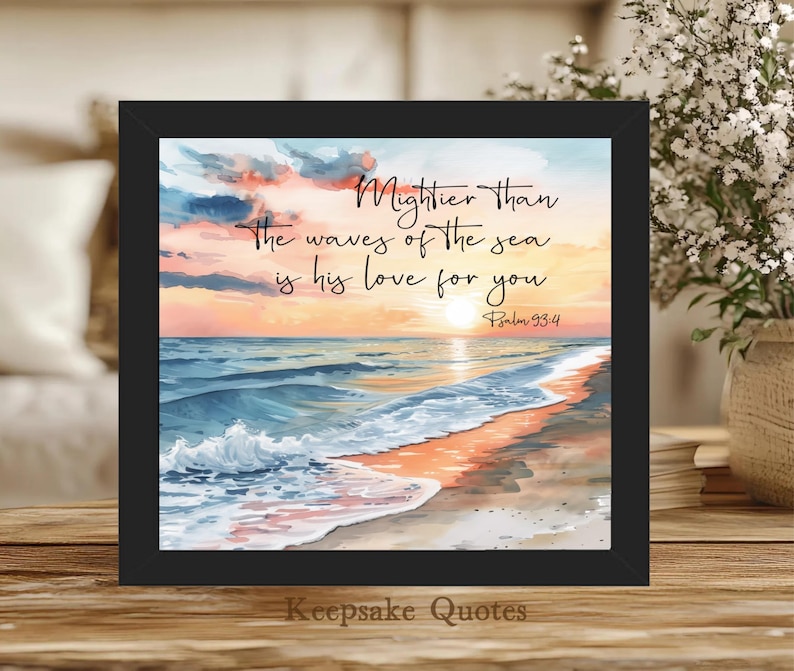 Op de afbeelding: Een ingelijste prent met een strandsc&egrave;ne bij zonsondergang. Het kunstwerk bevat de tekst "Mightier than the waves of the sea is his love for you" en "Psalm 93:4". De lijst is zwart en de prent is van "Keepsake Quotes".