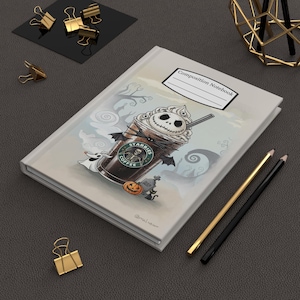 May include: A composition notebook with a Halloween-themed illustration. The design features a coffee cup with a Jack Skellington face, the text "Starbies Coffee", and other spooky elements. The notebook has a white cover with the words "Composition Notebook".
