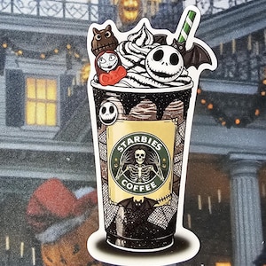 May include: A sticker featuring a spooky coffee cup design. The cup is filled with a dark liquid, whipped cream, and a green and white straw. The cup has a skeleton logo and the text "STARBIES COFFEE". The design includes characters from The Nightmare Before Christmas.