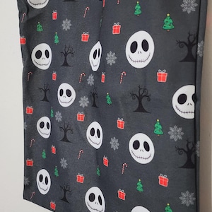May include: A gray tote bag featuring a pattern of Jack Skellington faces, Christmas trees, snowflakes, candy canes, and gift boxes. The bag has gray handles and is made of fabric.