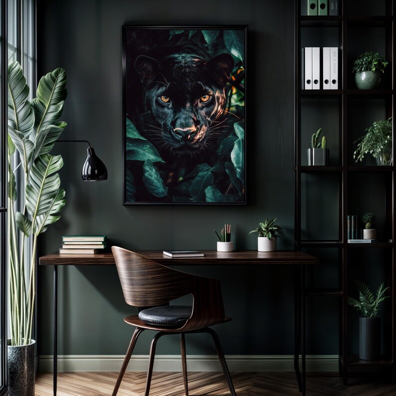 May include: Framed art print featuring a black panther peering out from lush green foliage. The panther's yellow eyes are the focal point. The artwork is displayed in a dark, modern interior with a desk, chair, and shelving unit.