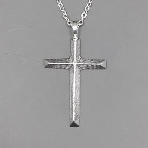 May include: A silver chain necklace with a textured silver cross pendant.