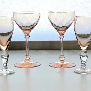 May include: Four vintage pink-tinted glassware pieces. Two have a coupe shape with diamond-cut bowls, and two are stemmed flutes. The glasses are displayed on a white surface with a light background.