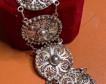May include: A silver filigree bracelet with four circular and oval decorative elements. Each element features intricate openwork patterns and a central silver bead. The bracelet is connected by small, delicate links.