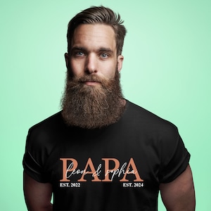 Può includere: Maglietta nera con il testo "PAPA Leon & Sophia EST. 2022 EST. 2024" in arancione.