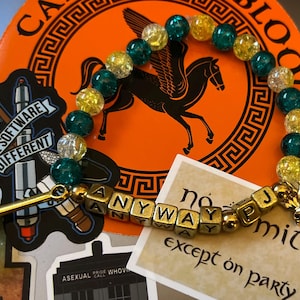 May include: A beaded bracelet with gold-colored letter beads spelling "ANYWAY" and "JP". The bracelet features teal, gold, and clear beads. A gold trident charm and a Pegasus sticker are also visible.