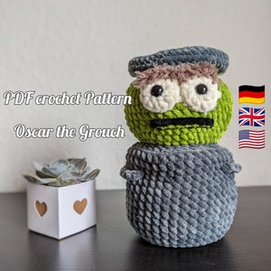 May include: Crochet pattern for Oscar the Grouch, a green and gray amigurumi doll with a grumpy expression. The pattern includes instructions for making the doll's body, head, and hat. The pattern is available in English, German, and American English.