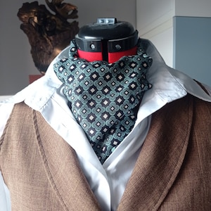 Puede incluir: Una corbata de patrón blanco y negro con un diseño turquesa. La corbata está atada alrededor de un cuello de camisa blanco y un chaleco marrón.