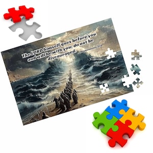 Op de afbeelding: Een puzzel met een schilderij van een groep mensen die over een strand lopen met een stormachtige zee op de achtergrond. De puzzel bevat de tekst "The LORD himself goes before you and will be with you; do not be discouraged. Deuteronomy 31:8".