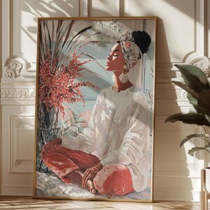 May include: A framed art print depicts a person in a white top and red pants, seated in a meditative pose. The artwork features a floral head wrap, large earrings, and a vase of red flowers. The background is a soft blue and white.