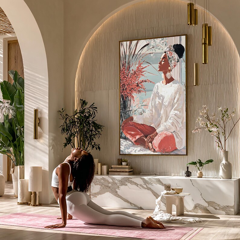 May include: A woman in a white sports bra and leggings performs a yoga pose on a pink mat. A large framed painting depicts a person in white clothing and red pants. The room has a modern design with plants and decorative lighting.
