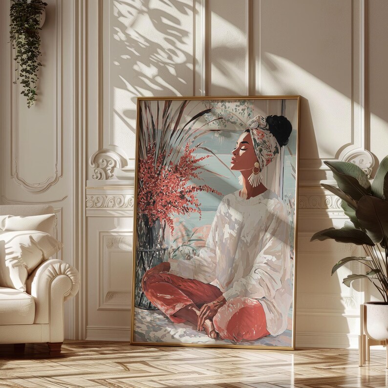 May include: A framed art print depicts a person in a white top and red pants, seated in a meditative pose. The artwork features a floral head wrap, large earrings, and a vase of red flowers. The background is a soft blue and white.