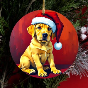 May include: A round Christmas ornament featuring a yellow Labrador puppy wearing a red and white Santa hat. The puppy is sitting against a solid red background. The ornament is suspended by a gold string and displays a detailed illustration.