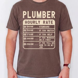 May include: A brown short-sleeve t-shirt featuring the text PLUMBER HOURLY RATE and a price list: 100/HR standard, 150/HR if you watch, 175/HR if you help, 200/HR if you worked on it first, and 250/HR if you tell me how to do my job.