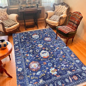 以下が含まれることがあります： 白い縁取りのある青い花柄の敷物。敷物は、2つの椅子とテーブルのあるリビングルームにあります。