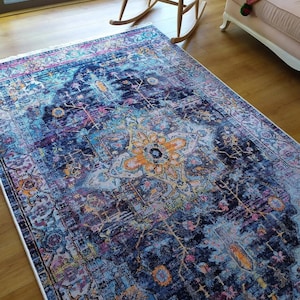 May include: A blue, pink, and yellow patterned rug with a floral design in the center. The rug has a white border and is made of a soft, plush material.