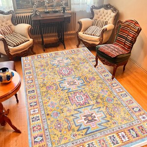 May include: A yellow, blue, pink, and red patterned rug with a geometric design. The rug is laid out on a wooden floor in a living room setting.