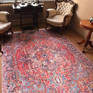 Puede incluir: Una alfombra con estampado rojo, azul y amarillo con diseños intrincados. La alfombra está colocada sobre un suelo de madera en un salón.