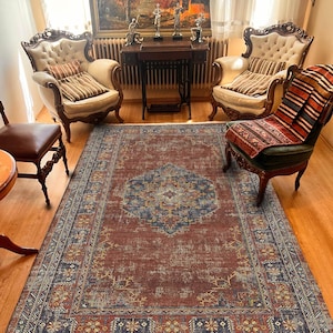 May include: A rectangular, distressed-look rug with a central medallion design in shades of blue and cream on a reddish-brown background. The rug features a detailed border with floral and geometric patterns, adding a vintage aesthetic to the room.