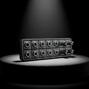 May include: A black rectangular electronic device with multiple circular input jacks and knobs. The device has two rows of five jacks each, with two knobs on the right side. The device is on a round, dark surface.