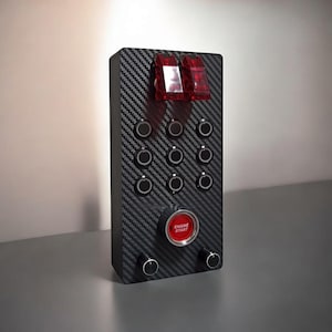 May include: A black panel with a carbon fiber pattern, featuring multiple round buttons, two red toggle switches, a red push button labeled "Engine Start", and two black knobs.