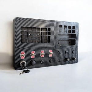 May include: A black control panel with a carbon fiber texture. It features multiple switches labeled "ON", a key lock, and various openings. The panel is designed for electronic devices and has a modern aesthetic.