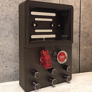 May include: A black panel with a carbon fiber pattern, featuring a red toggle switch, a red button labeled "Engine Start", and five black knobs.