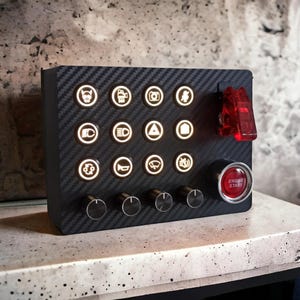 May include: A black panel with a carbon fiber texture features a variety of illuminated buttons and knobs. The buttons have icons for features like a camera, headlights, and a warning triangle. There is a red toggle switch and a red button labeled "Engine Start".