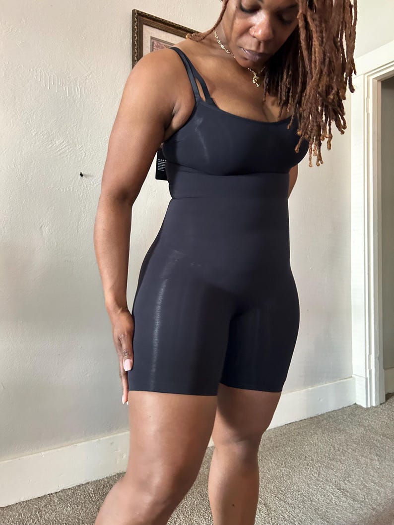 May include: Black bodysuit with spaghetti straps and shorts. The garment is form-fitting and appears to be made of a smooth, stretchy material. The bodysuit extends from the shoulders to mid-thigh.