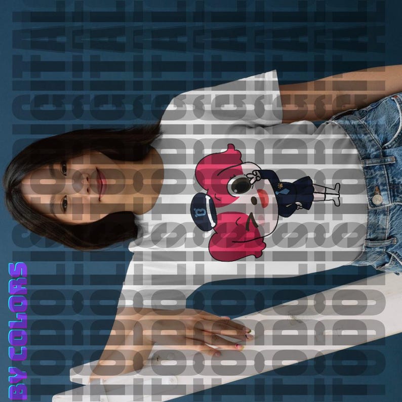 May include: White t-shirt featuring a cartoon illustration of a girl in a baseball cap and uniform. The girl has pink hair and is depicted in a playful pose. The design is printed on a white, short-sleeved t-shirt. The t-shirt is shown on a model, partially visible. The background is a blurred, dark blue color with repeating text. The overall style is casual and playful, suitable for everyday wear.