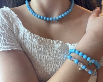 Puede incluir: Una mujer con una camisa blanca con un collar de cuentas azul claro y una pulsera de cuentas azul claro con un dije de plata.