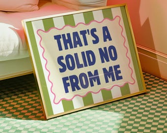 May include: A framed art print with the text "THAT'S A SOLID NO FROM ME" in blue letters. The frame has a gold border, and the print features a green and white striped border with a pink scalloped edge. The print is displayed near a white sofa.