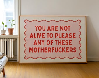 May include: A framed art print with the text "YOU ARE NOT ALIVE TO PLEASE ANY OF THESE MOTHERFUCKERS" in red on a pink background. The artwork is displayed in a room with a window, plants, and a wooden floor.