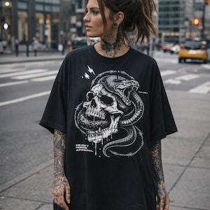May include: Black t-shirt with a white graphic of a skull and snake intertwined, with barbed wire details. The text "HEAVY INKED APPAREL" is printed below. The shirt has short sleeves and a loose fit, suitable for casual wear.