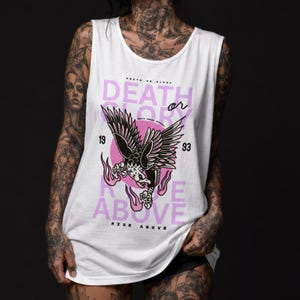 May include: White vest top with a graphic design. It features a black eagle with outstretched wings, a pink circle, and the words "DEATH or GLORY" and "RISE ABOVE". The vest top also has the numbers "19" and "93".